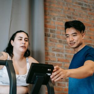 A personal trainer guiding a woman during an indoor cycling workout session.