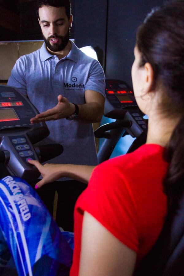 A personal trainer instructs a woman on using an exercise machine at the gym.